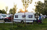Caravans and campers on green meadow in campsite. Sunrise, rays on campers in the morning. Green grass. Outdoor concept for traveling and res in the n...