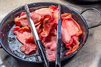 Pile of cooked back bacon in a serving skillet with tongs.
