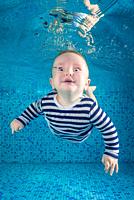 Little baby learns to swims underwater. Baby swimming underwater in the pool on a blue water background. Healthy family lifestyle and children water s...