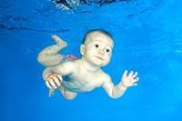 Little girl learns to swims underwater. Baby swimming underwater in the pool on a blue water background. Healthy family lifestyle and children water s...