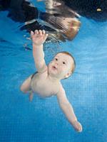 Little baby boy learning to swim underwater in a swimming pool.