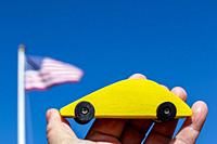 Yellow wooden car holding against blue sky with american flag.