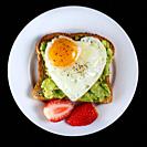 Toast with avocado and egg with heart shape on white plate isolated on black background.