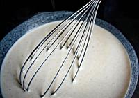 Metal whisk in a white liquid dough close up.