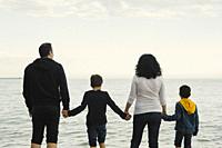 Family of four members standing on the beach and watching at the sea.
