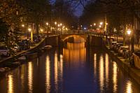 Reflections of bridge lighting in canals at dusk, Amsterdam, North Holland, Netherlands.