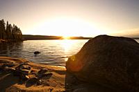 The golden sun is rising over an idyllic lake with large boulders on its shore on a clear day in autumn. Västernorrland, Sweden, Europe.