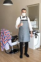 hairdresser prepared to cut hair in barbershop wearing face mask due to corona virus pandemic.