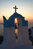 view of the sun at sunset through the bell tower of a typical church in oia santorini.