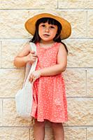 Portrait of a black-haired girl girl with summer dress, hat and bag.