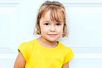 Adorable blond-haired girl wearing a yellow shirt leaning against white background.