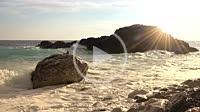 Sunny morning on the rocky shore. A wave is breaking against a rock with many splashes. Slow motion