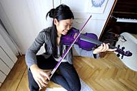 young asian girl playing the violin in her bedroom in Madrid (Spain)