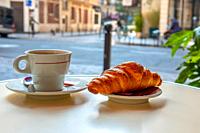 Table of street cafe in Paris in the morning. Cup of coffee and croissant close-up. Background in defocus.