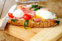 Bacon and poached eggs sandwich on the cut board.