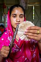 A woman making handicrafts is smoothing the fibers of a banana tree with scissors in Madhupur, Tangail, Bangladesh.