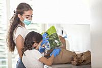 mother and daughter wears masks and gloves while taking out groceries.