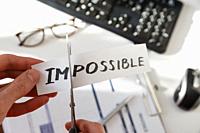 Businessman hands cutting the word impossible, letters im so it become possible. Success and motivation concept. On white.