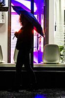 Stockholm, Sweden A woman with an umbrella walks by a tanning salon in Liljeholmen at night.