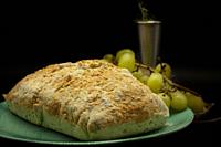 Freshly baked artisan bread made with parmesan cheese and rosemary next to grapes and fresh rosemary isolated on black background.
