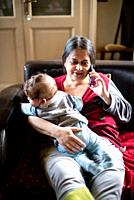 mother with little son in her arms, talking on smartphone sitting on the sofa.