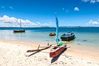 Malagasy outrigger pirogue with sail and boats on the white beach, Madagascar.