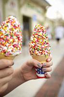 A pair of ice cream cones with sprinkles being held by a young girl's hands.