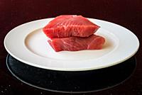 Fresh Tuna Steak on a white plate on a table as black background - fresh raw slices. Grain is the texture of the glass table.