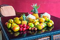 Fresh tropical Mauritius fruits on a purple glass table in the magenta background. The selection includes Coconut, Rose Apple, Mango and Pineapples.