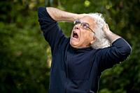 A grey haired 68 year old man making a face and pulling his hair out. ,.