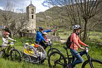 Family on bike and romanesque church of Sant Feliu, Barruera, Vall de Boí, Lleida, Catalonia, Spain.