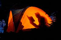 Silhouette Of A Man Reading A Book In A Tent in The Wilderness.