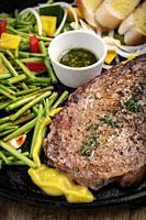 organic tenderloin beef steak sizzler on hot plate meal platter with mixed vegetables and chimichurri sauce.