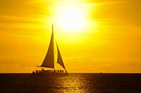 Sailboat with a group of people enjoying a golden sunset off the coast of Aruba, in front of Hadicurari Beach.