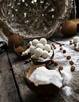 Coconut candy, balls, coconuts and hazelnuts on a rustic wooden surface.