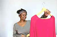 Portrait of young black woman with afro hairstyle with clothes on hangers indoor at home. Lifestyle concept.