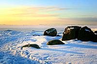 Snow covered rocks at the breakwater of the island of Särkkä, Helsinki, Finland with a footpath in snow. There is a waterway and lighthouse on the hor...