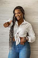 Portrait of a smiling African American adult woman standing doing thumb up and looking at the camera. Adult woman with black and yellow braids posing ...