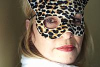 Portrait of a fifty plus years old woman with brown eyes wearing a fake leopard skin covered mask and bright red lipstick.
