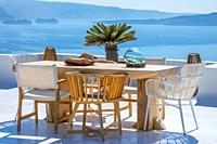 Greece. Santorini. Thira island. Wooden table and chairs on a sun terrace. Two cruise ships in the harbor.