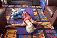A woman, 60+ years old, moves her legs to her side and spreads her arms out as she practices yoga in her apartment home, Windsor, Ontario, Canada.