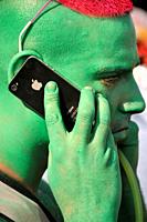 Portrait of young man, face painted in green color, hair painted in red color, talking by mobile phone, Lake Parade - LGBT Parade, Pride Parade, Genev...