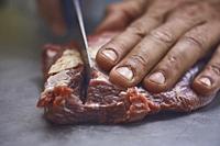 detail of the hand of a butcher intending to cut a piece of meat with the knife of which you notice very well the fibers and texture,.