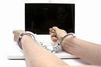 Outstretched arm of a woman with handcuffs to wrists on computer roof conceptual cyber crime.