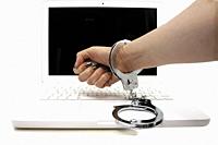conceptual cybercrime thief with handcuffed hand in front of white laptop clenching fist.