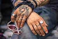 Tattooed hands posing while holding a pair of sunglasses.