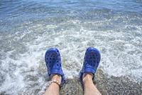Male wearing blue clogs beside the beach. Selective focus.