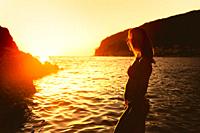 Beautiful woman in bikini looking at amazing sunset by the sea. Silhouette photo at golden hour.