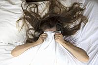 Young woman lying in bed suffering, tired woman covering face with hands, can't sleep feels exhaustand on white sheets in bedroom closeup.