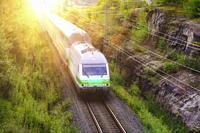 VR Intercity train travels at speed through rural landscape with green trees, elevated view. Salo, Finland. August 29, 2021.